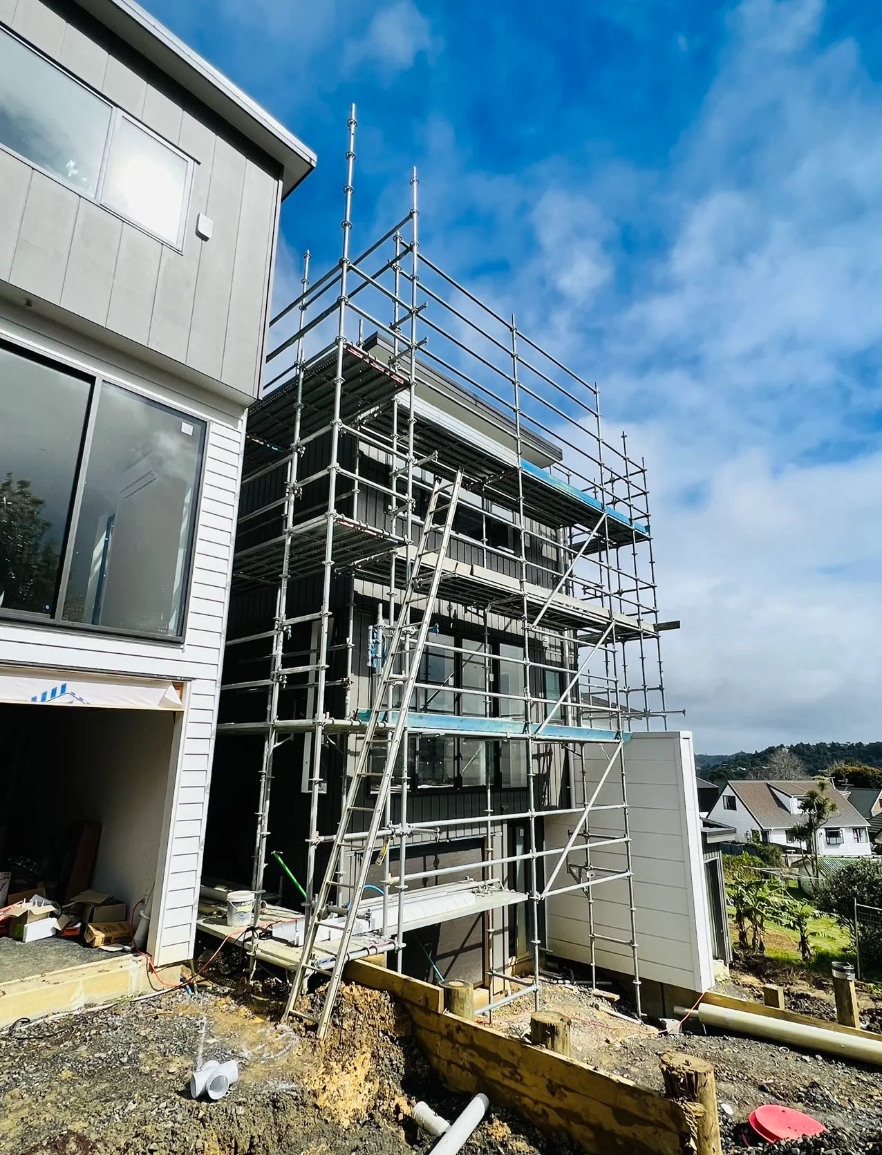 Construction site with extensive scaffolding systems in use, showing multiple levels of steel framework with workers in safety gear, blue sky background with modern building under construction